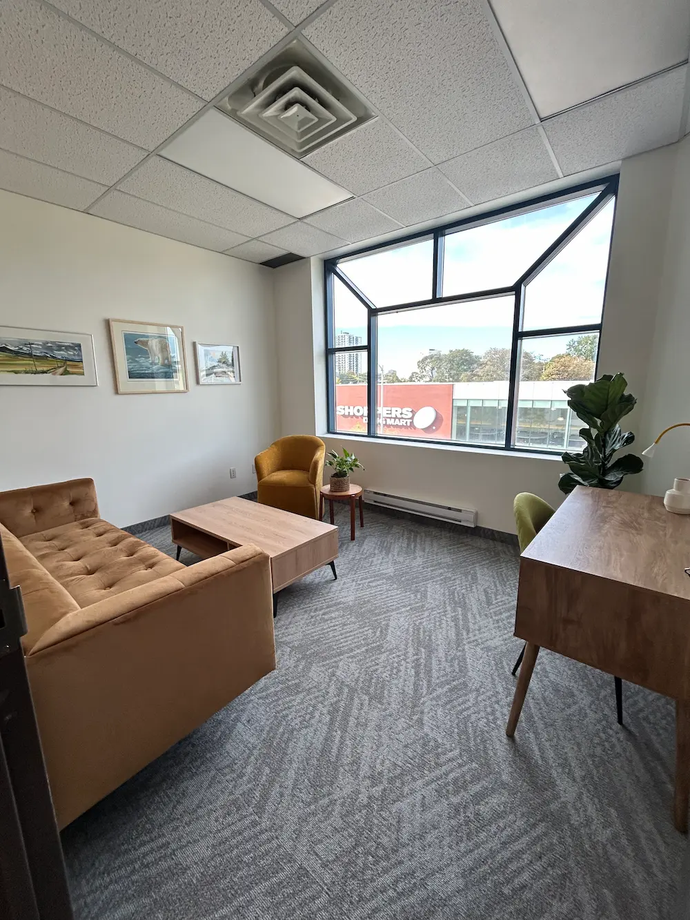 Bright therapy room with a velvet sofa and armchair beside a large corner window at the Riverdale office